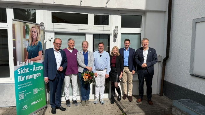 Begrüßung der neuen Landarztstarterin Dr. Doris Tenberge vor der Mentorenpraxis in Meschede, daneben ein Roll-up „Land in Sicht – Ärzte für morgen“